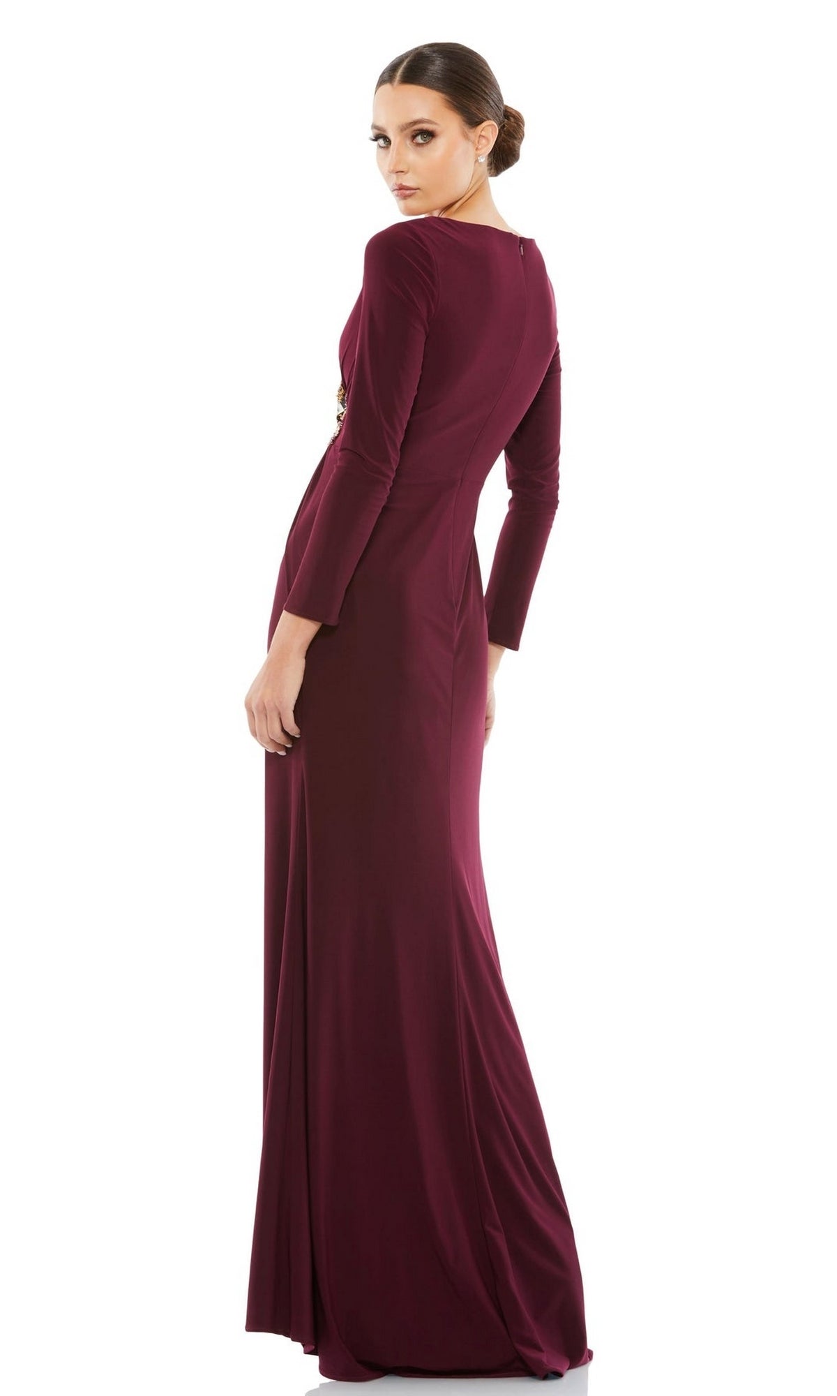 A woman models the Long Formal Dress 68736 by Mac Duggal, featuring a fitted silhouette, v-neckline, and elegant beaded applique, as she stands turned slightly to the side against a white background.